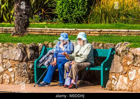 Two women friends chat together on a garden or park bench. Stock Photo
