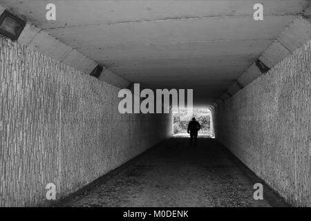 Looking through tunnel at figure in distance in black and white Stock Photo