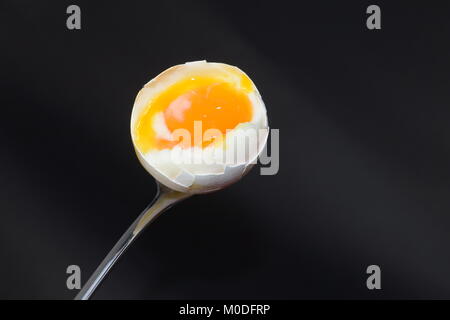 A opened, boiled egg on a silver spoon on a black background Stock Photo