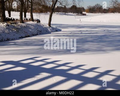 frozen snow covered lake with fence and trees shadows Stock Photo