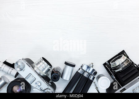 vintage retro photo cameras, tripod, negative film rolls and lens on white wooden surface background with copy space Stock Photo