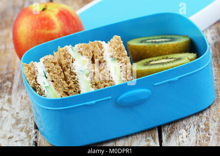 Healthy school lunch box containing brown cream cheese sandwiches, kiwi fruit and apple Stock Photo
