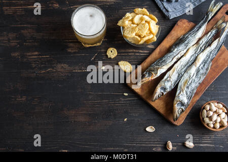 Assorted snacks for beer: sun dried fish, nuts, salted croutons or crackers over wooden background, top view, copy space. Lager beer and snacks, dried Stock Photo