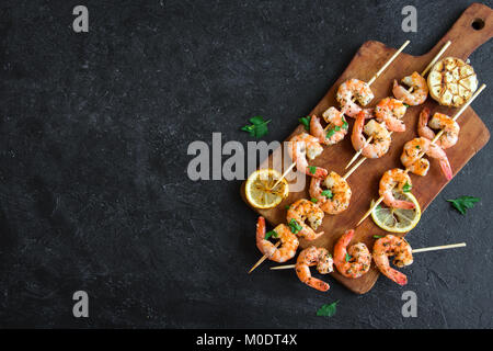 Grilled shrimp skewers. Seafood, shelfish. Shrimps Prawns skewers with herbs, garlic and lemon on black stone background, copy space. Shrimps prawns b Stock Photo