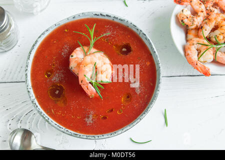 Vegetable tomato soup gazpacho with shrimps (prawns) and rosemary in bowl on white wooden background, top view, copy space. Stock Photo