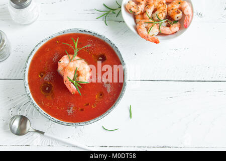 Vegetable tomato soup gazpacho with shrimps (prawns), olive oil and rosemary in bowl on white wooden background, top view, copy space. Stock Photo