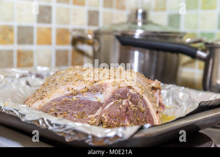 Closeup raw lamb leg joint on roasting tin foil with ingredients ready for roasting. Stock Photo