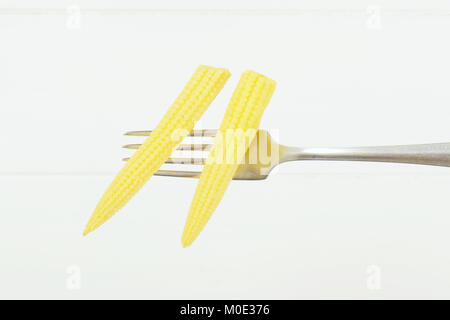 two cobs of sweet baby corn on metal fork Stock Photo