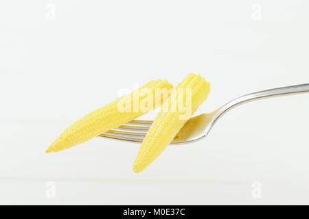 two cobs of sweet baby corn on metal fork Stock Photo