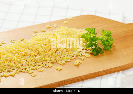 heap of uncooked alphabet pasta on wooden cutting board - close up Stock Photo