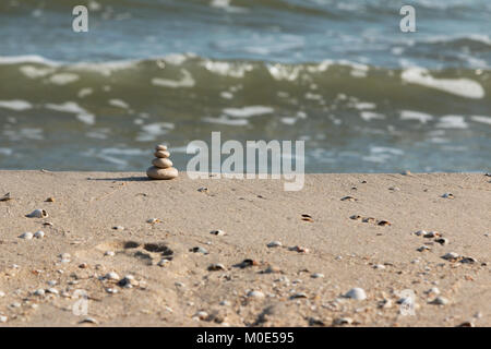Pyramid is made of white stones against the background of sea waves. Pebble stack on the seashore Stock Photo