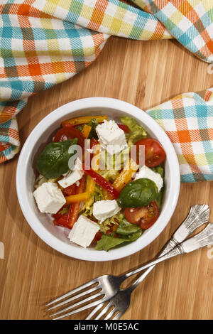 mediterranean salad with red and yellow paprika stripes, goat cheese cubes, cherry tomatoes and basil in a bowl
