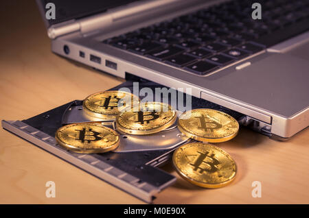 Physical bitcoins over a laptop's CD drive . Trading and mining concept of cryptocurrency Stock Photo