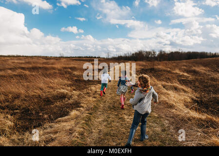 Three children running along a footpath in a rural landscape Stock Photo