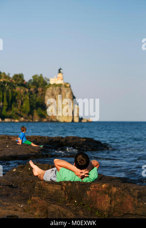 Father and son lying on rocks by a lake Stock Photo