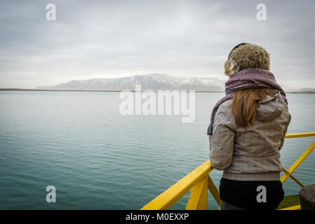 Woman looking at sea and snowy mountains from the yellow lighthouse in Reykjavik, Iceland. Stock Photo