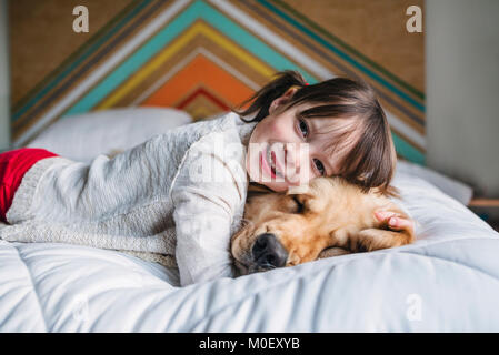 Girl lying on a bed with her golden retriever dog Stock Photo