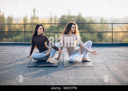 Two beautiful womei make corner posture with twisting, acroyoga on the roof outdoors. Girlfriends simultaneously perform a beautiful element of yoga.  Stock Photo