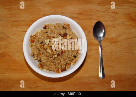 Oatmeal with raisins and chopped nuts in a white bowl on a wooden surface Stock Photo