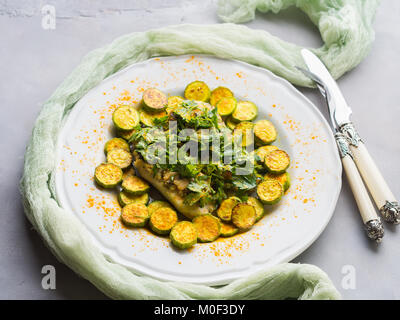 Baked Stock fish fillet with almond parsley topping and turmeric courgettes on white plate. Healthy diet dish Stock Photo