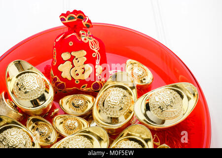 Chinese New year ang pow red felt fabric bag with gold ingots in red tray on white wood table top,Chinese Language on bag mean Happiness and on ingot  Stock Photo