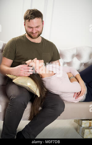 Young couple on the couch. A man and a woman look at each other with a loving glance. They are celebrating something. Under the couch are boxes with g Stock Photo