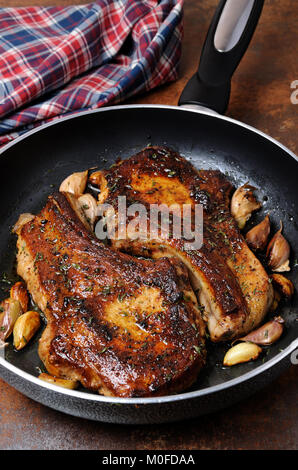 Fried pork chop on bones with herbs and garlic in a frying pan Stock Photo