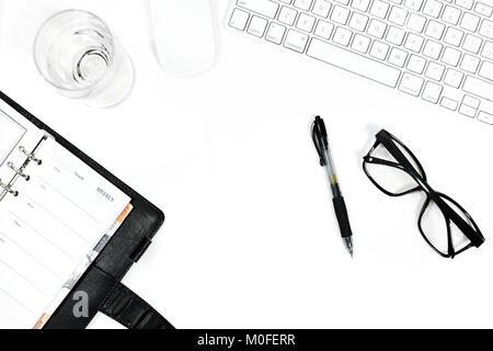 White office desk table with open diary,computer keyboard,computer mouse,spectacle,glass of water and pen.Top view with copy space,Flat Lay. Stock Photo