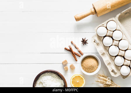 Baking ingredients on white table. White eggs, rolling pin, flour, sugar and spices. Home baking concept, baking cake or cookies ingredients Stock Photo