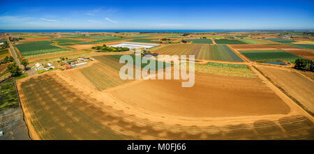 Aerial panorama of plowed fields and crops near ocean coastline on bright summer day. Werribee South, Victoria, Australia Stock Photo