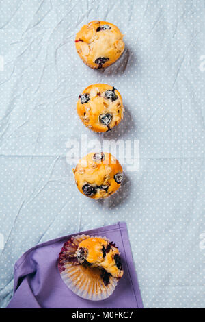 Freshly baked blueberry muffins with almond, oats and icing sugar topping in a row on a polka dots tablecloth. Top view. Stock Photo