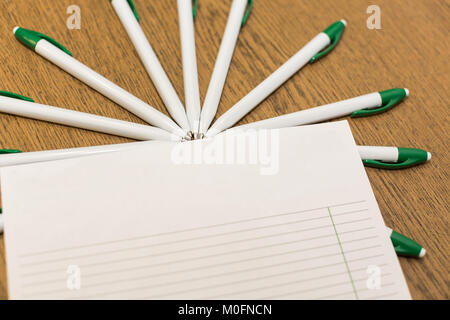 studing, educating, equipment concept. on the brown surface of school desk there is set of ballpoint pens, they are covere with clean piece of ruled p Stock Photo