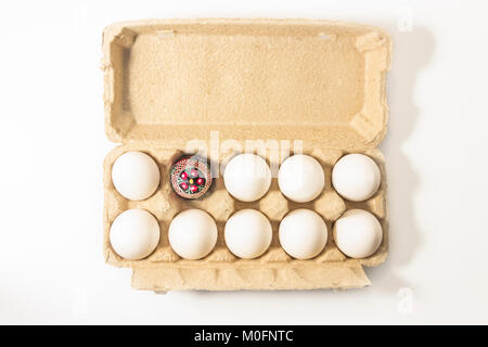 Handmade folk culture decorated easter egg packed in recycled cardboard box among white plain eggs. easter coming soon. Stock Photo