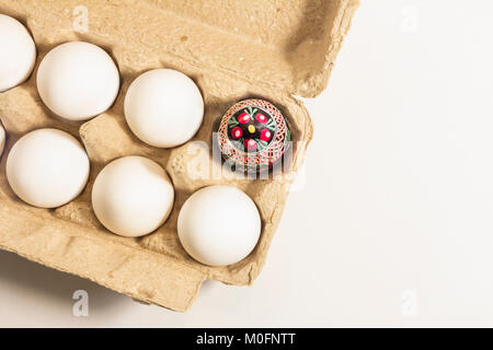 Handmade folk culture decorated easter egg packed in recycled cardboard box among white plain eggs. easter coming soon. Stock Photo