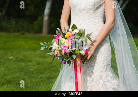 Wedding bouquet in bride hands closeup with colorful roses and peonies at green nature background Stock Photo