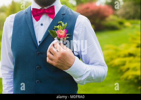 Fragment of luxury groom outfit in white shirt, blue cotton vest and pink details on the green outdoor background Stock Photo