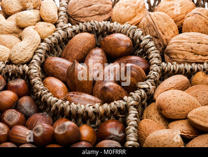 Basket reach in various kinds of nuts in shells, pecans, almonds, hazelnuts, peanuts and walnuts on white background Stock Photo