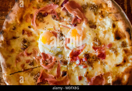 A breakfast pizza, with mozzarella cheese, cooked ham, sausage, and two fried eggs, sunnyside up Stock Photo