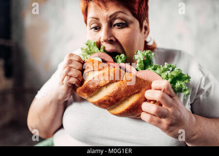 Fat woman eats sandwich, overweight and bulimic. Unhealthy lifestyle, obesity Stock Photo