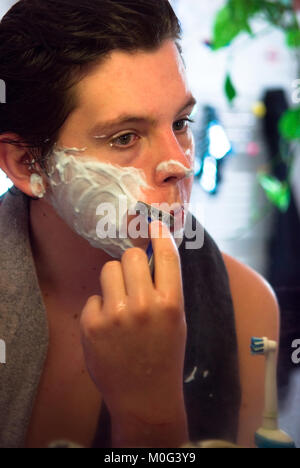 close up of attractive male teenager looking at himself in the mirror while he has his first wet shave Stock Photo