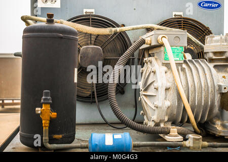 closeup of an old and rusty ac compressor and fan on top of the roof and the fan of the unit is in the background Stock Photo