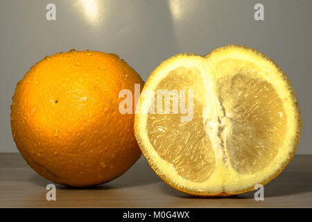 closeup of a slice of an fresh and healthy orange kept beside a big whole orange kept on a wooden table Stock Photo