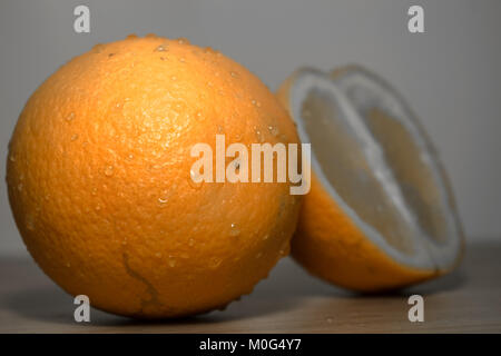 closeup of a slice of an fresh and healthy orange kept beside a big whole orange kept on a wooden table Stock Photo