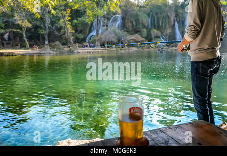 A young man fishing with rod and reel at the lake at Kravica or Kravice Falls in Bosnia and Herzegovina on a sunny fall afternoon Stock Photo