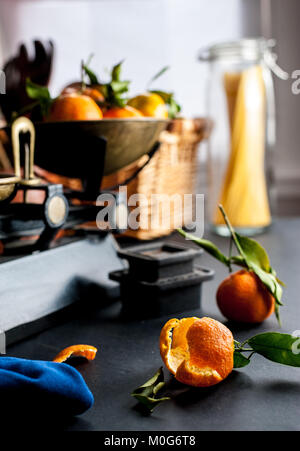 Fresh whole clementines with green leaves in vintage scale and one peeled clementine on a black table with a blue cloth and several weights Stock Photo