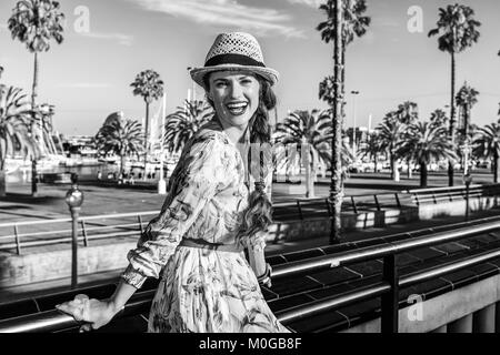 Summertime at colorful Barcelona. Portrait of smiling modern tourist woman in long dress and straw hat on embankment in Barcelona, Spain Stock Photo