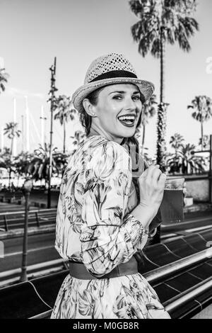 Summertime at colorful Barcelona. Portrait of smiling elegant tourist woman in long dress and straw hat on embankment in Barcelona, Spain with bright  Stock Photo