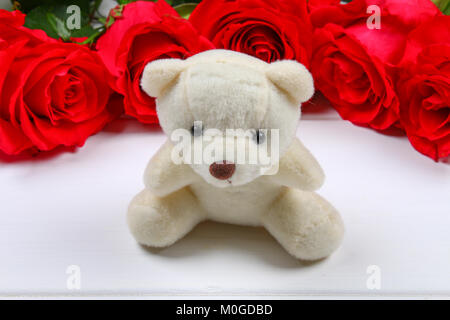 White teddy bear surrounded by pink roses on a white wooden table. Template for March 8, Mother's Day, Valentine's Day Stock Photo