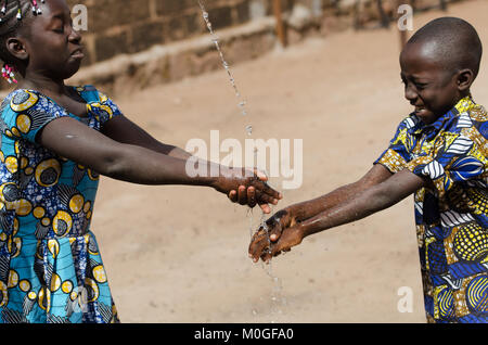 Two African Children Cleaning Hands Outdoors with Fresh Water Stock Photo