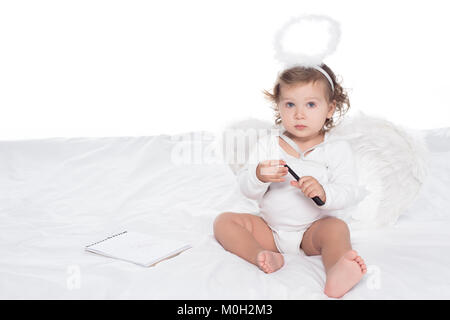 little angel with wings and nimbus on bed with notepad, isolated on white Stock Photo